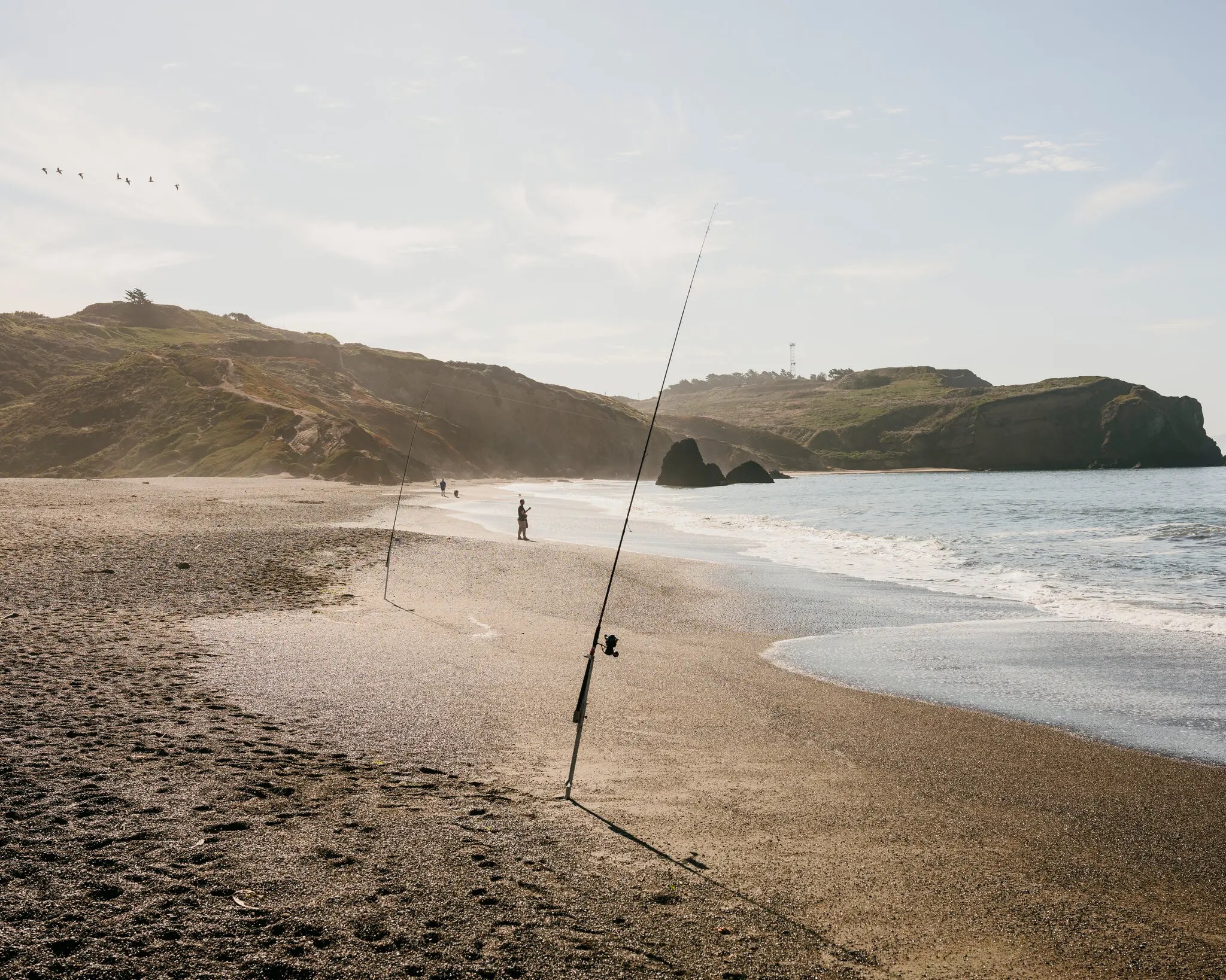 Fishing pole stuck in the sand on a gold sand beach in Northern Califronia. Coastal bluffs are seen in the background.