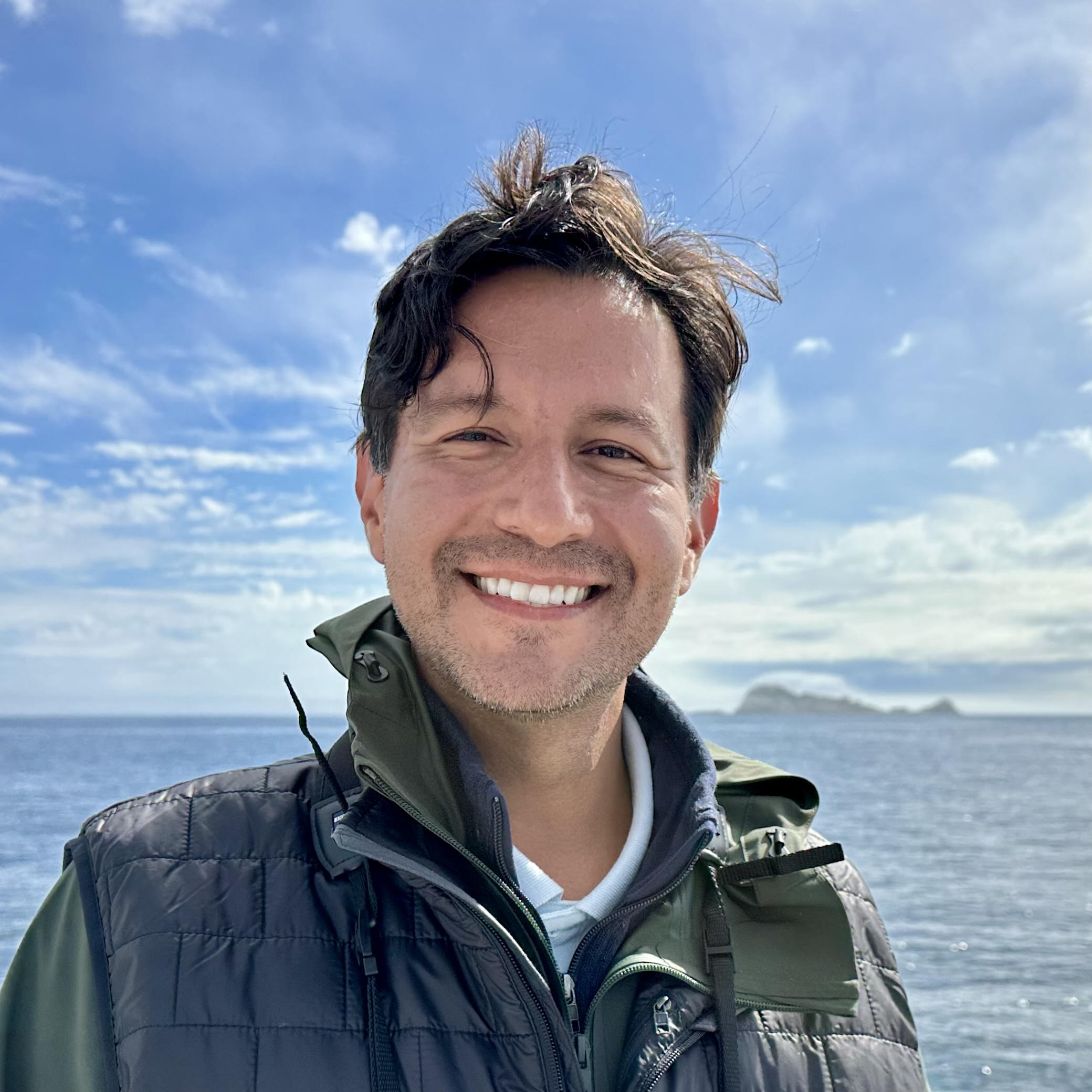 Adam stands in front of the Farallon Islands on a boat