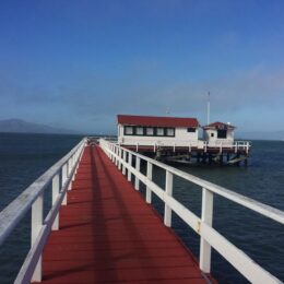 Photo the Greater Farallones Pier Classroom: white and dark red colored boat house at the end of a long pier atop the San Francisco Bay.