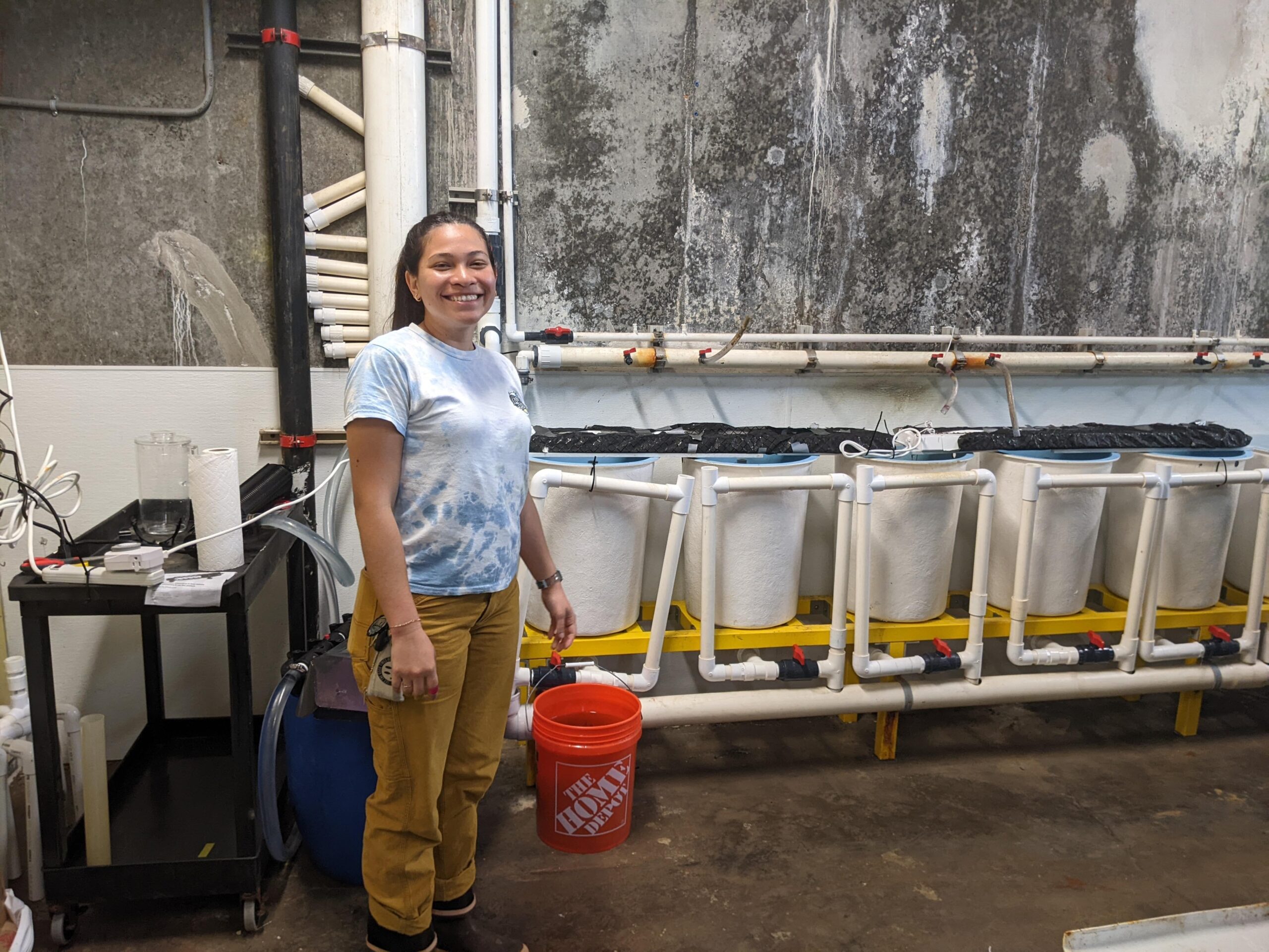 Julieta stands in front of gray, industrial looking kelp culturing tanks